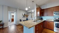 This single-floor residence offers a thoughtfully designed open layout that connects the kitchen, dining, and living areas seamlessly. The kitchen is equipped with rich warm-toned cabinetry, granite countertops, stainless steel appliances including a range and built-in microwave, a double-basin sink, and a peninsula with pendant lighting that overlooks the dining area — ideal for both cooking and entertaining. The dining space accommodates a full dining set and is accented with contemporary artwork and wood-look flooring that extends throughout the main living areas. The living room is bright and comfortable, featuring a sliding glass door that opens to a private balcony, a ceiling fan, and generous wall space. The primary bedroom offers plush carpeting, dual windows that invite natural light, a ceiling fan, and ample room. The second bedroom is equally well-lit with multiple windows. Two full bathrooms serve the residence: one featuring a soaking tub and shower combination with warm wood-tone cabinetry, and the second offering a walk-in glass-enclosed shower. Neutral-toned walls and consistent wood-look flooring throughout the main areas create a cohesive, modern aesthetic.