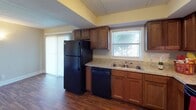 This single-story residence offers three bedrooms and two full bathrooms within a practical, well-organized floor plan. The kitchen serves as a functional hub, featuring warm wood cabinetry, light granite-style countertops, black appliances including a refrigerator, electric range, and dishwasher, alongside a double-basin sink positioned beneath a window that brings in natural light. The flooring throughout the kitchen and select rooms consists of hardwood-style planking, adding warmth and durability.

The bedrooms are carpeted and finished with neutral tones, each featuring windows fitted with blinds that allow for natural light and outdoor views. One bedroom includes access to adjoining spaces, suggesting a primary suite configuration with closet access. Textured ceilings are consistent throughout the home.

Both bathrooms are finished with neutral, earthy tones. One bathroom features a fully tiled walk-in shower with mosaic tile flooring, while the second bathroom includes a vanity with a granite-style countertop, wood cabinetry, a large mirror, and tile flooring. White trim and baseboards are consistent throughout, providing a clean, cohesive aesthetic across the entire residence.