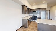 This efficiently designed single-floor unit on Centennial Trail in Arlington, Washington, makes thoughtful use of its compact footprint. Light wood-tone luxury vinyl plank flooring runs consistently throughout, creating a cohesive and clean aesthetic across all areas.

The kitchen is a standout feature, showcasing rich dark-espresso cabinetry extending to the upper walls, maximizing vertical storage. Light quartz countertops provide strong visual contrast, while a mosaic tile backsplash adds a decorative accent. A full suite of stainless steel appliances—including a refrigerator, range, microwave, and dishwasher—is integrated seamlessly. A central island with matching cabinetry offers additional prep and storage space.

The open living area is bright and neutral, with recessed lighting, clean white walls, and a wall-mounted utility panel. A paneled white door leads to the bathroom and laundry area.

The bathroom is notably spacious relative to the overall unit size, featuring dark-toned cabinetry with a dual-basin vanity, a large mirror, and a stacked washer and dryer unit conveniently housed within the same room, providing practical all-in-one functionality.