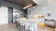 Located at 1111 Fairfield Ave in Cleveland's vibrant Ohio City neighborhood, this thoughtfully designed one-bedroom, one-bathroom residence offers a refined modern living experience. The open-concept floor plan seamlessly connects the kitchen, dining, and living areas, creating an efficient yet airy feel enhanced by light oak hardwood flooring throughout.

The chef's kitchen is a standout feature, showcasing a large waterfall-edge island with seating for multiple guests, sleek white flat-front upper cabinetry with under-cabinet lighting, contrasting dark lower cabinetry, stainless steel appliances including a French door refrigerator and professional range, and a dramatic dark ceiling detail framing the space.

The living room is bathed in natural light from expansive floor-to-ceiling windows with black frames, offering elevated views of the surrounding Cleveland cityscape. A built-in dark niche adds architectural contrast to the otherwise bright, white interior.

The bedroom continues the modern aesthetic with large windows that invite natural light and neighborhood views, complemented by clean white walls and light flooring. A dedicated closet provides practical storage.

The bathroom delivers a spa-like experience with a frameless glass walk-in shower clad in vertical tile, a sleek floating vanity, bold matte black fixtures, and an illuminated mirror, all set against deep charcoal walls for a striking, contemporary finish.