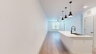 This well-designed one-bedroom, one-bathroom unit offers a thoughtfully laid-out single-floor plan with modern finishes throughout. The open-concept kitchen and living area serves as the heart of the unit, where light wood-look flooring, crisp white walls, and a ceiling fan create a clean, airy atmosphere. The kitchen is anchored by a substantial white island with an integrated sink and matte black faucet, complemented by a trio of black pendant lights overhead. White cabinetry, a subway tile backsplash, and stainless steel appliances — including a range and over-the-range microwave — complete the functional yet stylish kitchen. The living area extends naturally from the kitchen, featuring a window that allows natural light to filter in.

The bedroom is finished with plush carpeting, a ceiling fan, a large window with blinds, and a walk-in closet outfitted with multi-tiered shelving and hanging rods for generous storage. The bathroom features wood-look tile flooring, gray cabinetry with matte black hardware, a white countertop vanity, and a tub/shower combination with marble-style surround and a glass door. A dedicated laundry area and additional closet space round out this efficiently designed unit.