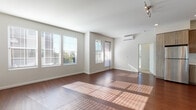 Located at 1335 Brookline Loop in Pleasanton, California, this single-floor residence offers a clean, modern aesthetic throughout. Rich hardwood-style flooring flows seamlessly through the main living areas, complemented by neutral walls that create a bright, welcoming atmosphere. The spacious main living area is bathed in natural light from an expansive arrangement of large windows fitted with horizontal blinds, offering views of the surrounding greenery. A wall-mounted mini-split climate control unit ensures year-round comfort. The open kitchen is thoughtfully designed with contemporary wood-grain cabinetry extending to the ceiling, light quartz countertops, a white tile backsplash, a stainless steel sink, and a full suite of stainless steel appliances including a gas range, over-range microwave, and dishwasher. Recessed lighting illuminates the kitchen area efficiently. The bathroom features hardwood-style flooring, a full soaking tub with shower, clean white surround, and a modern vanity with a lighted mirror and wood-grain cabinetry. A generously sized walk-in closet provides ample storage with a full-length hanging rod and carpeted flooring. The overall design of this residence balances functionality with modern style.