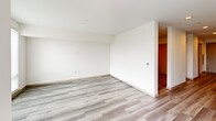 Located in the Queen Anne neighborhood of Seattle, WA, Unit 606 at 400 Queen Anne Ave N offers a well-designed, single-floor open layout. Light-toned luxury vinyl plank flooring runs throughout the entire unit, lending a clean, contemporary aesthetic that ties each area together seamlessly.

The kitchen is a standout feature, outfitted with light wood flat-panel cabinetry accented by matte black hardware, a white quartz countertop, and a subtle tile backsplash. A full suite of stainless steel appliances — including a refrigerator, electric range, over-the-range microwave, and a dishwasher — makes this a highly functional cooking space. A single-basin sink with a matte black faucet completes the setup. Large windows at the end of the kitchen corridor allow natural light to pour through into the adjacent living area.

The open living area provides a blank canvas for flexible furniture arrangements. Crisp white walls and recessed lighting contribute to a bright, airy atmosphere throughout.

The bathroom features a clean, minimalist design with a wood-toned vanity, white quartz countertop, a large wall mirror, and matte black fixtures and hardware. A soaking bathtub with an overhead shower rounds out the space, all set against white walls and matching plank flooring for a cohesive, modern finish.