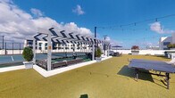 Located at 805 North Olive Avenue in West Palm Beach, Florida, this rooftop amenity deck offers a dynamic open-air recreational environment designed for active enjoyment and social gathering. The space is anchored by a dedicated pickleball court finished in a classic green surface, sheltered beneath a bold black-and-white geometric pergola that provides shade while maintaining the breezy, open atmosphere characteristic of South Florida living. Lush artificial turf covers a generous portion of the deck, creating a comfortable, low-maintenance lawn area that invites casual recreation, including a ping-pong table positioned for easy use. Overhead, bistro-style string lights are strung across the rooftop, lending a warm ambiance ideal for evening gatherings. Umbrella-shaded seating areas are arranged throughout the space, offering spots to relax and socialize with views of the surrounding West Palm Beach skyline and the bright blue Florida sky above. The clean, modern design of the deck is characterized by white architectural elements and well-defined zones for both active play and leisurely relaxation. The combination of recreational amenities, thoughtful shade structures, and stylish lighting makes this rooftop deck a compelling and versatile outdoor destination.