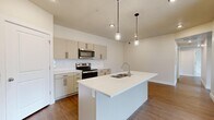 This well-designed single-story home offers three bedrooms, two bathrooms, and a thoughtfully laid-out floor plan that maximizes functionality throughout. The open-concept kitchen and living area serves as the heart of the home, featuring a central island with an undermount sink and pendant lighting overhead. The kitchen is outfitted with taupe cabinetry, white quartz countertops, a classic subway tile backsplash, and a full suite of stainless steel appliances including a range and over-the-range microwave. Warm hardwood-style flooring runs throughout the main living areas, lending a cohesive and contemporary feel. The three bedrooms are carpeted for comfort, with large windows that bring in generous natural light and offer open outdoor views of the surrounding landscape. The primary bedroom includes a walk-in closet with built-in shelving and dual hanging rods for ample storage. Both bathrooms are finished with white cabinetry, quartz countertops, and hardwood-style flooring; one features a full tub-shower combination. A dedicated laundry room accommodates a full-size washer and dryer. The overall aesthetic is clean and modern, with neutral tones and quality finishes throughout.