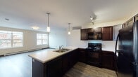 This single-floor unit offers a thoughtfully designed open-concept layout that seamlessly connects the kitchen and living area. The kitchen is a standout feature, showcasing rich dark-wood cabinetry with ample storage, light countertops, a peninsula with an integrated sink, and a full suite of black appliances including a refrigerator, range, microwave, and dishwasher. Elegant pendant lighting hangs above the peninsula and track lighting above the range, adding both function and style. The kitchen flows naturally into a spacious living area finished with durable hardwood-style flooring and multiple windows that invite natural light and provide outdoor views of the surrounding neighborhood.

Two well-proportioned bedrooms are finished with plush carpet flooring, large windows with blinds, and baseboard heating, creating a comfortable and quiet retreat. The unit includes two bathrooms, each featuring hardwood-style flooring, dark vanity cabinetry, light countertops, a large mirror, and clean, neutral wall tones. One bathroom includes a walk-in closet area. A wall-mounted mini-split HVAC unit in the main living area provides efficient climate control. Throughout the unit, warm beige walls, dark trim accents, and consistent finishes create a cohesive and modern aesthetic.