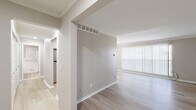 This 2-bedroom, 1-bathroom single-floor residence offers a clean, neutral aesthetic with a practical and cohesive layout. The combined kitchen and living area anchors the unit, with the living room benefiting from large floor-to-ceiling vertical blinds that flood the space with natural light and light wood-style flooring that extends throughout the main areas. Crown molding adds a refined touch to the living room's clean lines.

The kitchen is well-equipped with white shaker-style cabinetry, brushed nickel hardware, a stainless steel sink, stone-look countertops, and a stainless steel refrigerator, all set atop matching light wood flooring. A closet adjacent to the kitchen provides convenient additional storage.

Both bedrooms are carpeted in a warm neutral tone, offering a comfortable and quiet retreat. The primary bedroom is generously sized with a dedicated closet featuring built-in shelving. A second bedroom provides flexible space for various uses.

The bathroom is bright and functional, featuring white tile wainscoting, a single-sink vanity, a soaking tub with shower, and a window dressed with vertical blinds for natural light. Two hallways connect the spaces efficiently, contributing to a smooth flow throughout. Overall, the unit presents a bright, move-in-ready environment with consistent finishes.