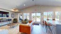 Located at 93 E Tahoe St in Oak Creek, Wisconsin, this single-floor community clubhouse is thoughtfully designed to serve as a social and recreational hub. The main lounge area is highlighted by soaring vaulted ceilings, recessed lighting, and warm hardwood-style flooring, creating an open and welcoming atmosphere. Stylish furnishings, including a tufted leather sofa and curated artwork, lend the space a contemporary yet comfortable character. Large glass doors and expansive windows flood the interior with natural light and provide direct views of the outdoor pool area, seamlessly connecting indoor and outdoor living. The well-appointed kitchen features white shaker cabinetry, quartz countertops, stainless steel appliances, and a coffee station, making it ideal for resident gatherings. A dedicated game room offers shuffleboard and foosball tables alongside patterned carpeting and neighborhood views. A private workstation nook provides a functional retreat with a live-edge wood desk and printing amenities. Additional flexible spaces include a media lounge with a mounted television. A fully equipped fitness center rounds out the amenities, offering residents a comprehensive wellness facility within the community.