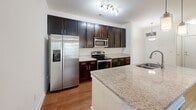 Located at 2022 Proximity Dr in Charleston, SC, this single-story home offers four bedrooms and two bathrooms within a well-organized floor plan. The open-concept kitchen and living area serves as the heart of the home, featuring rich dark-espresso cabinetry, granite-look countertops, stainless steel appliances including a range, microwave, and refrigerator, and warm hardwood-style flooring. A central kitchen island with a built-in sink and pendant lighting adds both functionality and visual appeal. Track lighting overhead enhances the kitchen's brightness.

The living room is carpeted and filled with natural light through a large window, complemented by a ceiling fan for added comfort. A door from the living area provides outdoor access. The four bedrooms are finished with neutral carpet and light-toned walls, offering versatile, move-in-ready spaces. The primary bedroom is generously proportioned.

Both bathrooms are finished with diagonal-set tile flooring, dark vanity cabinetry, white countertops, framed mirrors, and tiled tub-shower combinations. A dedicated laundry room houses full-size washer and dryer units with built-in shelving above. The home also includes a hallway and additional closet storage, rounding out a practical and comfortable layout.