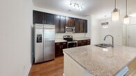 Located at 2022 Proximity Dr in Charleston, SC, this single-story home offers four bedrooms and two bathrooms within a well-organized floor plan. The open-concept kitchen and living area serves as the heart of the home, featuring rich dark-espresso cabinetry, granite-look countertops, stainless steel appliances including a range, microwave, and refrigerator, and warm hardwood-style flooring. A central kitchen island with a built-in sink and pendant lighting adds both functionality and visual appeal. Track lighting overhead enhances the kitchen's brightness.

The living room is carpeted and filled with natural light through a large window, complemented by a ceiling fan for added comfort. A door from the living area provides outdoor access. The four bedrooms are finished with neutral carpet and light-toned walls, offering versatile, move-in-ready spaces. The primary bedroom is generously proportioned.

Both bathrooms are finished with diagonal-set tile flooring, dark vanity cabinetry, white countertops, framed mirrors, and tiled tub-shower combinations. A dedicated laundry room houses full-size washer and dryer units with built-in shelving above. The home also includes a hallway and additional closet storage, rounding out a practical and comfortable layout.