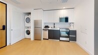 Located on the 7th floor at 3920 W 5th St in Los Angeles, this modern unit offers a thoughtfully designed single-level layout with clean lines and a bright, contemporary aesthetic throughout. Light oak hardwood flooring flows seamlessly across the living spaces, complemented by crisp white walls and recessed lighting that create an airy, open atmosphere.

The kitchen is efficiently appointed with stainless steel appliances, including a refrigerator, dishwasher, and range, alongside sleek two-tone cabinetry featuring white uppers and charcoal lowers, and a classic white subway tile backsplash. A stacked washer and dryer unit is conveniently integrated within the kitchen area.

Two well-proportioned bedrooms offer comfortable retreats, each with light-filled interiors and closet storage. One bedroom enjoys large windows with views of the surrounding Los Angeles cityscape, including palm trees and skyline elements, filling the room with natural light. A bold teal entry door adds a distinctive design accent near this bedroom, accompanied by a stone-topped built-in counter.

The bathrooms are finished with large-format neutral tiles. One features a glass-enclosed walk-in shower with matte black fixtures and a floating sink, while the second includes a vanity with a stone countertop. A smart thermostat is also present, reflecting the unit's modern conveniences.