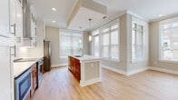Located at 5350 Pinehurst Park Dr in Charlotte's 28211 zip code, this single-floor residence combines modern finishes with a functional, open layout. The kitchen serves as a central highlight, featuring a large island with a white quartz countertop, an undermount sink, and pendant lighting overhead. Cabinetry blends warm wood lower cabinets with white upper cabinets accented by glass-front doors and cross-detail trim. A herringbone tile backsplash frames the stainless steel range beneath a sleek wall-mounted hood vent, while a stainless steel French door refrigerator and dishwasher complete the appliance suite. The kitchen opens to a bright dining or living area bathed in natural light from multiple windows with horizontal blinds. Light hardwood flooring flows consistently throughout the living areas and bedrooms, creating a cohesive and airy feel. Bedrooms are well-proportioned with natural light and access to walk-in closets. The bathrooms are finished with large-format marble-look tile flooring, white shaker-style vanities with quartz countertops, and brushed nickel hardware. The primary bath includes a glass-enclosed walk-in shower, while the secondary bath offers a tub-shower combination. Neutral warm-gray walls throughout tie the entire space together cohesively.
