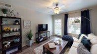 This single-floor residence offers a thoughtfully designed layout that balances comfort and functionality throughout its interconnected living spaces. The kitchen is outfitted with gray cabinetry, granite-style countertops, black appliances including a refrigerator, range, and built-in microwave, as well as a double sink and track lighting overhead. Wood-look flooring ties the kitchen seamlessly into the adjacent dining area, which features a bold teal accent wall adorned with decorative mirrors, creating a stylish focal point. The living room is bright and welcoming, with wood-look flooring, a ceiling fan, and a glass sliding door that fills the space with natural light and provides access to an outdoor area. The bedroom is carpeted and generously sized, highlighted by a deep teal accent wall, a ceiling fan, large windows with a sliding door to a private balcony, and direct access to a spacious walk-in closet. The bathroom is finished with gray cabinetry, granite-style countertops, a well-lit vanity mirror, and a separate tiled tub and shower combination. Consistent gray tones, warm wood accents, and coordinated navy and teal décor throughout contribute to a cohesive and contemporary ambiance.