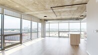 This contemporary high-rise unit offers an industrial-modern aesthetic across a single floor of thoughtfully designed living space. The open-plan living, dining, and kitchen area is the heart of the home, anchored by dramatic floor-to-ceiling glass walls that flood the interior with natural light and frame expansive panoramic city views. The exposed concrete ceiling with visible ductwork adds a raw, loft-like character, while light hardwood flooring provides a warm counterbalance throughout. The kitchen features a substantial island with light wood cabinetry and white countertops, complemented by stainless steel appliances and sleek white upper cabinets. Sliding doors with a modern track system offer seamless transitions between spaces. The three bedrooms are well-proportioned, with the primary bedroom benefiting from its own floor-to-ceiling windows and generous closet space. Four closets total provide ample storage throughout the unit. The three bathrooms are finished with warm-toned tile flooring, light wood vanities, and matte black hardware accents. A dedicated laundry room houses a stacked washer and dryer unit. Two hallways connect the living areas to the private quarters, ensuring a practical and intuitive layout throughout.