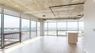 This contemporary high-rise unit offers an industrial-modern aesthetic across a single floor of thoughtfully designed living space. The open-plan living, dining, and kitchen area is the heart of the home, anchored by dramatic floor-to-ceiling glass walls that flood the interior with natural light and frame expansive panoramic city views. The exposed concrete ceiling with visible ductwork adds a raw, loft-like character, while light hardwood flooring provides a warm counterbalance throughout. The kitchen features a substantial island with light wood cabinetry and white countertops, complemented by stainless steel appliances and sleek white upper cabinets. Sliding doors with a modern track system offer seamless transitions between spaces. The three bedrooms are well-proportioned, with the primary bedroom benefiting from its own floor-to-ceiling windows and generous closet space. Four closets total provide ample storage throughout the unit. The three bathrooms are finished with warm-toned tile flooring, light wood vanities, and matte black hardware accents. A dedicated laundry room houses a stacked washer and dryer unit. Two hallways connect the living areas to the private quarters, ensuring a practical and intuitive layout throughout.