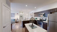 Located at 2100 East Aventura Way in St. Louis, MO, this 2-bedroom, 2-bathroom residence offers a thoughtfully organized single-floor layout. The open kitchen is outfitted with dark espresso cabinetry, light quartz countertops, stainless steel appliances including a range, microwave, and refrigerator, and wood-look flooring that extends throughout the main living areas. A kitchen island provides additional counter and storage space. The living room is bright and welcoming, featuring a ceiling fan, a large window dressed with grommet curtains that invite natural light, and wood-look flooring. The primary bedroom is generously sized, featuring plush carpet, a spacious double-door closet, and a clean, neutral palette. The second bedroom also offers carpeted flooring and a window with natural light. The primary bathroom includes a walk-in shower with glass doors, a dark-vanity with a vessel sink, and open industrial shelving. The second bathroom features a full tub-shower combination and a matching dark-toned vanity. An entry area with built-in cabinetry and double closet doors provides a practical and welcoming arrival point. Throughout the residence, the design maintains a consistent modern aesthetic with neutral tones and clean finishes.