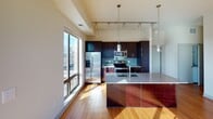 Located in Minneapolis's vibrant Whittier neighborhood, this well-appointed unit at 2839 Emerson Ave S offers a thoughtfully designed single-floor layout with a contemporary aesthetic. The open-concept living area is anchored by rich hardwood flooring and benefits from abundant natural light streaming through large sliding glass doors that lead to a private balcony, offering sweeping views of the surrounding Minneapolis cityscape. A ceiling fan and track lighting add functional style to this generous main living space.

The kitchen is a standout feature, showcasing dark espresso cabinetry, granite countertops, and a tiled backsplash in a cool blue-green hue. A center island with a built-in sink provides additional workspace and casual dining potential, while stainless steel appliances—including a French door refrigerator with ice maker, electric range, and microwave—complete the modern finish. Pendant lights and track lighting illuminate the space effectively.

The bedrooms are carpeted for comfort and feature large windows that frame urban views, filling each room with natural light. The bathrooms are finished consistently with tile flooring, dark vanity cabinetry, white countertops, and full tub-shower combinations, providing a clean and functional design throughout.