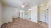 This single-story unit is designed with a practical, open layout that connects the kitchen and living areas seamlessly. The living space is finished with wall-to-wall carpet in a neutral tan tone and features ceiling fans with light fixtures, contributing to a comfortable, well-ventilated atmosphere. The open floor plan allows for flexible furniture arrangements across the generously sized main living area.

The kitchen is positioned adjacent to the living space and is equipped with warm-toned wood cabinetry, white appliances including a refrigerator, electric range, built-in microwave, and dishwasher. Light tile flooring and a window above the sink provide natural light to the workspace. Counter space runs along two walls in an L-shaped configuration, offering functional storage and prep areas.

The bedrooms are carpeted and include ceiling fans, wall-unit HVAC systems for individual climate control, and windows with blinds that allow natural light and outdoor views. Crown molding adds a refined detail to one bedroom.

The bathroom features tile flooring, a full-size soaking tub with a shower, white fixtures, and warm wood cabinetry above the toilet, providing practical storage. The overall palette throughout the unit is neutral and clean, creating a move-in ready environment.