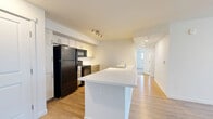 This single-floor, 2-bedroom, 2-bathroom residence at 1750 Greeley Mall in Greeley, Colorado offers a clean, modern design with a practical and comfortable layout. Light wood-style luxury vinyl flooring runs throughout the main living areas, complementing the bright, white walls and creating a fresh, cohesive aesthetic.

The kitchen is a standout feature, showcasing a generous island with a white countertop and built-in sink, warm wood-toned lower cabinetry, white upper cabinets, and black appliances including a refrigerator, range, and dishwasher. Track lighting and recessed fixtures keep the space well-lit. The kitchen flows naturally toward a hallway connecting the rest of the home.

The living room is open and airy, with access to a private balcony through a glass door flanked by vertical blinds. A wall-mounted HVAC unit provides climate control, and the room receives natural light from the balcony-facing window.

Both bedrooms feature soft carpeting, ceiling fans, and ample closet space, including a sliding-door closet in the primary bedroom. The two bathrooms are finished consistently, with wood-toned vanity cabinetry and white countertops. One bathroom offers a full tub-shower combo, while the other features a spacious vanity. In-unit laundry and three closets round out this well-organized home.
