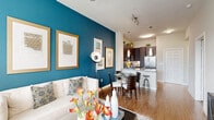 Located in Houston's prestigious Galleria corridor, this one-bedroom, one-bathroom residence offers a thoughtfully designed open-concept layout finished with warm hardwood flooring throughout. The living room serves as the centerpiece of the home, highlighted by a bold teal accent wall, expansive windows that frame city skyline views, and a ceiling fan that adds both function and style. Natural light fills the space generously, creating a bright and welcoming atmosphere. The kitchen is well-appointed with rich dark-espresso cabinetry, granite countertops, stainless steel appliances including a refrigerator, microwave, and range, a tile backsplash, and a peninsula with bar seating — ideal for casual dining. An adjacent dining area provides additional space for entertaining. The bedroom is a comfortable retreat featuring hardwood floors, large windows with city views, and ample closet space across three closets. The bathroom is clean and functional, featuring a walk-in shower with tile surround. A hallway connects the living spaces efficiently, adding to the home's practical flow. The overall design balances contemporary aesthetics with everyday livability in a prime Houston location.