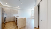 Located at 1085 Goldstream Ave in Victoria, BC, this thoughtfully designed single-floor unit offers a clean, contemporary aesthetic throughout. The open-concept kitchen and living area forms the heart of the space, finished with warm wood-look luxury vinyl plank flooring that runs seamlessly underfoot. The kitchen is well-appointed with light wood-grain cabinetry extending to the ceiling for generous storage, a white quartz peninsula countertop with a double stainless steel sink, and a full suite of stainless steel appliances including a refrigerator, range, over-the-range microwave, and dishwasher. Recessed lighting illuminates the kitchen area, while crisp white walls keep the atmosphere bright and open. The living area benefits from a large window and a glass-panel door that opens directly onto a private balcony, inviting natural light and views of surrounding greenery. The bathroom is finished to match the unit's modern palette, featuring wood-grain cabinetry with a white countertop vanity, a full soaker tub and shower combination with white surround, and coordinating wood-look flooring. The overall ambiance is clean, neutral, and move-in ready, reflecting a consistent modern design sensibility throughout.