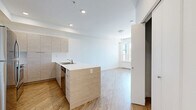 Located at 1085 Goldstream Ave in Victoria, BC, this thoughtfully designed single-floor unit offers a clean, contemporary aesthetic throughout. The open-concept kitchen and living area forms the heart of the space, finished with warm wood-look luxury vinyl plank flooring that runs seamlessly underfoot. The kitchen is well-appointed with light wood-grain cabinetry extending to the ceiling for generous storage, a white quartz peninsula countertop with a double stainless steel sink, and a full suite of stainless steel appliances including a refrigerator, range, over-the-range microwave, and dishwasher. Recessed lighting illuminates the kitchen area, while crisp white walls keep the atmosphere bright and open. The living area benefits from a large window and a glass-panel door that opens directly onto a private balcony, inviting natural light and views of surrounding greenery. The bathroom is finished to match the unit's modern palette, featuring wood-grain cabinetry with a white countertop vanity, a full soaker tub and shower combination with white surround, and coordinating wood-look flooring. The overall ambiance is clean, neutral, and move-in ready, reflecting a consistent modern design sensibility throughout.