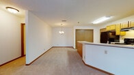 Located at 1579 S Moorland Rd in New Berlin, Wisconsin, this single-floor unit offers a functional and straightforward layout designed for comfortable everyday living. The open-concept living and dining area is finished with neutral carpet and white walls, creating a bright, clean backdrop throughout. A modest chandelier anchors the dining space, adding a simple decorative touch. The curved kitchen peninsula separates the kitchen from the living area while maintaining an open feel. The kitchen features warm oak cabinetry, light countertops, tile flooring, and a full suite of black appliances, including a refrigerator, range, and dishwasher. A dedicated entry door provides direct access to the kitchen area. The bedroom is generously proportioned, with carpet flooring and a multi-pane window that allows natural light to filter in. A hallway connects the bedroom to the rest of the unit, with access to two bathrooms. The full bathroom includes an oak vanity with a single sink, tile flooring, and a tub-shower combo with sliding glass doors. A second, more compact bathroom offers an oak vanity and tile flooring. Consistent warm wood trim and neutral tones unify the overall aesthetic throughout the space.