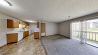 Located at 2011 W Bingham St in Ozark, Missouri, this single-floor, one-bedroom, one-bathroom unit offers a practical and well-organized layout. The open-concept living and dining area features plush carpet flooring, neutral gray walls, a textured ceiling, and a sliding glass door that floods the space with natural light and provides access to a private outdoor patio. A floor vent and entry door are also found in this area, contributing to a functional flow throughout.

The kitchen is efficiently designed with warm-toned oak cabinetry — both upper and lower — offering ample storage. It is equipped with white appliances including a coil-burner range, over-the-range microwave, dishwasher, and refrigerator. Light-toned countertops and a double-basin sink complete the workspace, all set over durable stone-pattern vinyl tile flooring that continues through the dining area.

The bedroom is a comfortable, carpeted retreat featuring a large sliding-door closet, a window with natural light, and a textured ceiling. An adjacent utility and laundry area adds everyday convenience.

The full bathroom includes a vanity with oak cabinetry, a lighted mirror, a toilet, and a tub/shower combination. Throughout the unit, consistent warm wood trim and neutral tones create a cohesive, understated aesthetic.