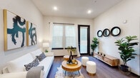 This contemporary single-floor residence at 8733 Rooks Park Cir in Tampa, Florida offers a well-designed layout with modern finishes throughout. The open-concept kitchen serves as a central highlight, featuring a large granite-topped island with pendant lighting, stainless steel appliances including a French door refrigerator, electric range, built-in microwave, and dishwasher. White upper cabinetry contrasts elegantly with dark lower cabinets, complemented by a subway tile backsplash and a deep undermount sink. Wood-look flooring runs seamlessly throughout the entire space, adding warmth and continuity. The living area is bright and inviting, with large windows and a glass door that allow generous natural light while offering outdoor access. Crisp white walls and recessed lighting create a clean, modern ambiance. The bedroom is a comfortable retreat featuring a substantial window with sheer draping curtains, dark wood-trim accents, and ample room for furnishings. The bathroom is well-appointed with a granite vanity, dark-framed mirror, and wood-look flooring, and opens directly into a spacious walk-in closet with built-in shelving. Overall, the space delivers a cohesive modern aesthetic with quality finishes and functional design.