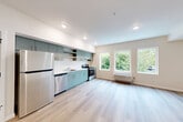 Located at 401 Union Ave SE in Olympia, Washington, this efficiently designed studio unit offers a well-organized, single-level layout that makes smart use of every square foot. The open-plan kitchen and living area forms the heart of the space, finished with light-toned luxury vinyl plank flooring that runs throughout, lending a clean and cohesive feel. The kitchen is outfitted with distinctive sage-green cabinetry—both upper and lower—paired with white countertops and a full suite of stainless steel appliances, including a refrigerator, dishwasher, and electric range with an overhead vent hood. Recessed lighting illuminates the kitchen and living zones, while a wall-mounted HVAC unit provides climate control. The living area is bathed in natural light courtesy of a bank of large windows that frame lush, green tree views, creating a calm and inviting atmosphere. Three closets provide generous storage throughout the unit. The combined bathroom and laundry room features a full soaking tub with shower, a vanity, and wood-look tile flooring consistent with the rest of the unit's palette. White Shaker-style interior doors, clean wall finishes, and a neutral color scheme give the entire space a modern yet understated character.