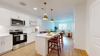 Located in Austin, TX, this well-designed one-bedroom, one-bathroom residence offers a thoughtful open-concept layout that maximizes comfort and functionality. Light wood-look flooring runs throughout the main living areas, creating a warm, cohesive feel.

The kitchen is a standout feature, outfitted with crisp white shaker cabinets, white quartz countertops, a classic subway tile backsplash, and a full suite of stainless steel appliances including a refrigerator with ice maker, range, microwave, and dishwasher. A central kitchen island with seating serves as both a prep space and casual dining area, illuminated by a pair of striking gold pendant lights.

The kitchen flows seamlessly into the living room, which benefits from natural light through a large window overlooking the outdoors. A ceiling fan adds to the comfort of the space.

The bedroom is a quiet retreat with plush carpet flooring, a ceiling fan, and a window that brings in natural light. The bathroom features wood-look flooring, a white vanity, and a full shower-tub combination. An adjacent walk-in closet provides generous storage space.

Clean white walls and modern finishes throughout lend the home a bright, contemporary ambiance well-suited for Austin living.