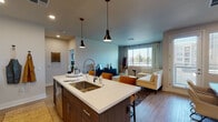 This single-floor residence showcases a thoughtfully designed open-concept layout that seamlessly connects the kitchen, dining, and living areas. The kitchen serves as a central hub, anchored by a large island with a white quartz countertop, an undermount sink, and stylish pendant lighting overhead. Two-tone cabinetry pairs dark lower cabinets with white upper cabinets, complemented by a classic subway tile backsplash. Stainless steel appliances, including a French door refrigerator, gas range, built-in microwave, and dishwasher, complete the well-equipped space.

The living room receives generous natural light through large windows dressed with sheer curtains and horizontal blinds, offering views of the surrounding area. Light wood-tone flooring flows consistently throughout, lending warmth and cohesion to the open floor plan. A dedicated dining area accommodates a full-sized table and is accented by a striking large-format wall art piece.

The bathroom features a white vanity with quartz countertop, a framed mirror, and a glass-enclosed walk-in shower, all finished in a clean, neutral palette. The entry area includes a spacious double-door closet, providing ample storage. Overall, the space presents a contemporary and well-coordinated aesthetic.