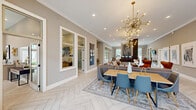 Located at 380 Topwater Dr in Clayton, NC, this single-floor community clubhouse offers a thoughtfully designed interior that blends modern aesthetics with functional comfort. The entrance welcomes visitors with herringbone-patterned light tile flooring and crown molding, setting an elegant tone throughout the space. The open-concept living and dining area serves as the heart of the clubhouse, anchored by a striking Sputnik-style brass chandelier that adds a bold contemporary focal point. The living area features a sleek fireplace flanked by decorative woven egg chairs and a cognac leather accent chair, complemented by curated abstract wall art. Large floor-to-ceiling glass doors and expansive windows flood the space with natural light and provide direct views of the outdoor pool area. A dedicated dining space offers a solid wood table with modern blue chairs, while a secondary dining room provides a quieter setting with a wall-mounted TV, ample natural light, and continued pool views. Built-in cabinetry with a neutral countertop offers additional utility in a neatly appointed nook. Neutral gray walls, white trim, and recessed lighting unify the design, creating a polished and inviting atmosphere throughout.