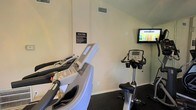 Located at 2945 Layfair Dr. in Flowood, Mississippi, this single-floor fitness center offers a dedicated space for cardio exercise and general wellness. The room features a dark, low-pile carpet flooring that is practical for a workout environment, while neutral-toned walls and overhead ventilation contribute to a clean, functional atmosphere. The facility is equipped with multiple treadmills and a stationary exercise bike, each outfitted with digital display consoles for tracking workout metrics. A wall-mounted flat-screen television is positioned at an optimal viewing height, allowing users to stay entertained during their workouts. A clearly visible "Fitness Rules" sign is posted on the wall, providing guidelines to ensure a safe and respectful environment for all users. The space is efficiently laid out to maximize the use of the available floor area while maintaining comfortable spacing between equipment. Ventilation is provided through ceiling vents, helping to maintain air circulation throughout exercise sessions. Overall, this fitness center provides a straightforward and well-equipped environment suited for residents or members looking to maintain an active lifestyle.