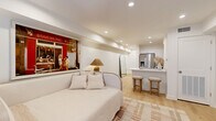 This thoughtfully designed single-floor space offers an efficient and stylish layout that maximizes every square foot. The open-concept living and kitchen area serves as the heart of the home, featuring light hardwood flooring throughout and recessed lighting that creates a bright, welcoming ambiance. The kitchen is outfitted with white shaker cabinetry, sleek white quartz countertops, stainless steel appliances including a French door refrigerator, and a peninsula with bar-height seating — ideal for casual dining or entertaining.

The generous bedroom is accessed through the main living area and features French doors with slatted blinds that allow for natural light control, along with recessed lighting and continued hardwood flooring. A dedicated closet provides practical storage. The space is completed by a full bathroom featuring large-format tile flooring, a tub-shower combination with bold navy subway tile surround, and built-in shelving for added convenience.

Throughout the space, a neutral, warm color palette — soft whites, warm beiges, and natural wood tones — creates a cohesive and calming aesthetic. The layout flows logically from the open living and kitchen zone into the private sleeping quarters, making this an efficient and inviting space.