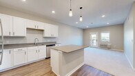 Located at 776 Hilaria Ave in Grand Junction, Colorado, this well-designed one-bedroom, one-bathroom unit offers a thoughtful layout across a single floor. The open-concept kitchen and living area serves as the heart of the home, featuring white shaker cabinetry with matte black hardware, gray quartz-style countertops, a stainless steel sink, and a full suite of stainless steel appliances including a refrigerator, range, microwave, and dishwasher. A central kitchen island with pendant lighting above provides additional prep space and anchors the transition into the carpeted living area. The living room is bright and spacious, with access to a private balcony through a glass-paned door, offering views of the surrounding landscape and distant mountains. The bedroom is generously sized with soft carpet, a large window framing outdoor views, and a wall-unit HVAC system for year-round comfort. Three closets provide ample storage throughout the unit. The bathroom is finished with a white vanity, gray countertop, undermount sink, a large mirror, and a full tub/shower combo, all set on warm wood-look flooring. A dedicated laundry area and hallway complete the functional floor plan.