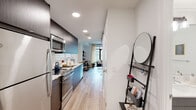 This well-designed single-floor residence offers a cohesive blend of modern aesthetics and functional living spaces. The open-concept layout connects the kitchen, dining, and living areas, creating a seamless flow throughout the unit. Light hardwood flooring runs consistently across the main areas, contributing to a warm and unified look.

The galley-style kitchen is outfitted with dark wood cabinetry, white quartz countertops, and a classic subway tile backsplash. Stainless steel appliances — including a range, microwave, and dishwasher — are integrated neatly into the cabinetry, maximizing both style and efficiency.

The living area is bright and airy, anchored by floor-to-ceiling windows that invite generous natural light and offer views of the surrounding urban landscape. The expansive glazing creates an open, connected feel with the outdoors.

The bedroom features a bold charcoal accent wall that adds depth and character to the space, complemented by light walls and hardwood flooring. A built-in closet provides practical storage.

The bathroom maintains the modern design language with large-format white tile flooring, a floating dark wood vanity with a white countertop, and a well-lit mirror. Clean white walls and efficient use of space give the room a crisp, contemporary finish. The entryway provides a functional transition point into the unit.