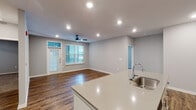 This single-floor residence showcases a thoughtfully designed open-concept layout that seamlessly connects the kitchen and living areas. The kitchen serves as a central focal point, featuring a large island with a light quartz countertop and an integrated sink, white shaker-style cabinetry, a classic subway tile backsplash, and stainless steel appliances including a refrigerator, range, and microwave. Recessed lighting illuminates the space throughout.

The living area extends naturally from the kitchen, finished with rich wood-style flooring, soft gray walls, and a ceiling fan. A glass-paneled exterior door paired with an adjacent window allows natural light to fill the room.

The bedrooms are carpeted for comfort, each offering windows with blinds that bring in ample natural light. A spacious walk-in closet with built-in shelving and hanging rods provides generous storage. The bathrooms feature wood-style flooring, light cabinetry with gray countertops, and a full tub-shower combination with tiled surround. A second bathroom offers an elongated vanity layout with additional storage. Neutral gray tones carry consistently throughout, contributing to a clean, modern aesthetic.