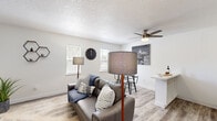 This single-story unit offers an efficient and well-designed layout that maximizes its compact footprint. The open-plan living area seamlessly integrates the living room, dining space, and kitchen, creating a cohesive and functional environment. Light wood-look flooring flows throughout, while textured ceilings and ceiling fans add character to the living and bedroom spaces. Multiple windows allow natural light to brighten the interior, enhancing the clean white walls and neutral palette.

The kitchen is outfitted with white cabinetry extending to the ceiling for ample storage, a stainless steel sink, and white appliances including a refrigerator and range. A compact dining area adjacent to the kitchen provides a dedicated space for meals. The living room offers enough space for a sofa and accent furniture, with a front entry door along one wall.

The bedroom accommodates a full-sized bed and features a ceiling fan, a sliding glass door leading to an outdoor area, and access to a dedicated walk-in closet equipped with wire shelving and hanging rods. The full bathroom includes a single vanity with a mirrored medicine cabinet and a shower-tub combination, finished in a clean, neutral style.