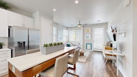 Located in Queen Creek, Arizona, this thoughtfully designed single-story, one-bedroom, one-bathroom home offers a clean, modern aesthetic with an efficient and well-organized layout. The open-concept design seamlessly connects the kitchen, dining area, and living room, creating a bright and airy atmosphere throughout. Wide-plank wood-look flooring flows consistently across the main living spaces, adding warmth and continuity.

The kitchen is a standout feature, outfitted with crisp white cabinetry, quartz countertops, a full suite of stainless steel appliances including a French door refrigerator, range, microwave, and dishwasher, and a central island with seating — ideal for casual dining. Multiple windows fitted with blinds allow ample natural light to fill the space.

The living room benefits from large corner windows, a ceiling fan, and direct access to an exterior door, making it feel open and connected to the outdoors. The bedroom is a comfortable retreat, highlighted by an arched accent wall, a large window, ceiling fan, and a closet for storage. The bathroom features a white vanity with quartz countertop, a glass-enclosed shower, and clean, contemporary finishes throughout. A dedicated hallway connects the private spaces with ease.
