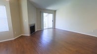 This single-floor space combines comfortable living with clean, functional design. The main living area is immediately welcoming, showcasing rich, dark hardwood flooring that runs throughout and lends a warm, polished character to the space. Neutral-toned walls provide a versatile backdrop, complementing the flooring and creating a bright, airy atmosphere. A fireplace serves as a natural focal point in the living area, adding a classic architectural detail that enhances the room's sense of comfort and charm. Large sliding glass doors flood the interior with abundant natural light and provide direct access to an outdoor balcony, where views of the surrounding environment can be enjoyed. The vaulted ceiling adds a sense of vertical space and openness that elevates the overall ambiance of the room. The layout is open and unobstructed, allowing for flexible furniture arrangements and a seamless flow throughout the space. Overall, this well-appointed single-floor space offers a harmonious blend of natural light, classic architectural features, and warm finishes that create an inviting and livable environment.