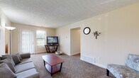 Located at 4334 Appian Way W in Columbus, Ohio, this single-floor home offers a comfortable and functional layout with a neutral, warm color palette throughout. The carpeted living room is a welcoming central space, featuring a textured ceiling, a large window that allows natural light to pour in, and an open passageway connecting to adjacent areas. The dining area is finished with wood-style flooring and includes a ceiling fan with integrated lighting, making it a bright and practical space for everyday meals. The kitchen is equipped with oak-toned cabinetry, a double-basin sink, light countertops, and a black dishwasher, with wood-style flooring continuing underfoot. A dedicated bedroom provides a quiet retreat, featuring plush carpet, a window with blinds, and a textured ceiling. An additional room, currently used as a children's space, also features carpet and a window with natural light. The full bathroom is finished with tile flooring and includes a vanity with oak cabinetry, a mirrored medicine cabinet, and a shower/tub combination. The entry area features wood-style flooring and a paneled wood door, providing a tidy transition into the home's interior.