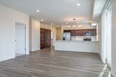 This well-appointed single-floor residence offers a clean, contemporary aesthetic throughout. The open-concept living and dining area is anchored by light-toned hardwood-style flooring and bathed in natural light through expansive floor-to-ceiling windows and a sliding glass door that opens to a private balcony with outdoor views. Vertical blinds and horizontal window treatments provide flexible light control throughout the main living space.

The kitchen is a standout feature, equipped with rich dark-wood cabinetry, stainless steel appliances including a side-by-side refrigerator, gas range, and microwave, complemented by crisp white quartz countertops. A built-in wine rack adds a refined touch, while a generous peninsula with pendant lighting separates the kitchen from the living area, making it ideal for both everyday functionality and entertaining.

The bedrooms feature soft wall-to-wall carpeting, ample closet space, and large windows that allow natural light and outdoor views. Interior doors throughout are modern flat-panel style with brushed nickel hardware. The bathroom is finished with a frameless sliding glass shower enclosure, brushed chrome fixtures, and decorative patterned tile flooring, offering a polished and spa-like feel. Recessed lighting and a neutral color palette unify the space with a bright, airy atmosphere.