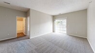 This single-floor unit is designed with a practical and comfortable layout. The living area is generously proportioned, featuring neutral-toned carpet and a sliding glass door that invites natural light while offering a view of the surrounding exterior. The open feel is enhanced by textured ceilings and clean white baseboards throughout the carpeted rooms.

The kitchen is functional and well-equipped, featuring white cabinetry, light wood-look flooring, and a full suite of stainless steel appliances including a refrigerator, range, and over-the-range microwave. Adjacent areas transition seamlessly between the kitchen and living spaces.

The bedrooms are carpeted and finished in soft neutral tones, with each room offering adequate space and natural light from windows fitted with blinds. A ceiling fan is present in one bedroom. The bathroom includes a full tub-shower combination, wood-look tile flooring, and taupe-toned walls, providing a clean and utilitarian finish.

A dedicated laundry area houses a full-size washer and dryer alongside wire shelving for added storage, rounding out this well-organized, move-in-ready space.