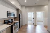 Located at 100 Hemenway Street in Boston's Fenway neighborhood, this model two-bedroom, one-bathroom unit offers a thoughtfully designed layout across a single floor. The open-concept kitchen, dining, and living area serves as the heart of the home, finished with light wood-style flooring that creates a warm, cohesive feel. The kitchen is outfitted with a full suite of stainless steel appliances — including a refrigerator, range, microwave, and dishwasher — complemented by white upper cabinetry, gray lower cabinets, and light stone countertops. Recessed lighting throughout keeps the space bright and modern.

The two bedrooms feature plush carpeting and crisp white walls. The primary bedroom includes a wall-mounted mini-split system for climate control and closet access, while the second bedroom benefits from a curved bay window arrangement that invites generous natural light. Three closets throughout the unit provide ample storage.

The bathroom is finished with large-format gray floor tiles, white subway tile in the walk-in shower, a wood-toned vanity with a white countertop, and brushed nickel fixtures — a clean, contemporary aesthetic overall. This unit offers a functional and stylish layout well-suited for urban Boston living.