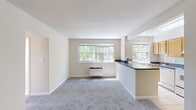 This single-floor, 2-bedroom, 1-bathroom residence offers a practical and well-organized layout designed for comfortable everyday living. The open-concept living area is bright and inviting, featuring plush carpet flooring and multiple large windows that frame lush greenery views, allowing natural light to fill the space throughout the day. A wall-mounted heating unit keeps the living area comfortable year-round.

The kitchen is efficiently designed with warm honey-toned wood cabinetry, dark granite-style countertops, and a peninsula that opens toward the living area, creating a connected, functional flow. White appliances including a range, refrigerator, and sink are neatly arranged, and light tile flooring adds a clean, practical touch. Overhead lighting illuminates the workspace effectively.

Both bedrooms are carpeted and feature neutral wall tones, individual windows with outdoor views, and built-in closet storage. The primary bedroom includes a wide bi-fold closet, while the second bedroom offers a single closet and natural light via a well-positioned window.

The bathroom is finished with classic white tile, a tub-shower combination, a window with blinds offering garden views, and a clean, functional layout. A hallway connects the private rooms to the main living spaces, completing this thoughtfully arranged residence.
