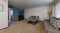 This single-floor home at 1915 N Porter Ave in Wichita, Kansas, offers a well-organized layout with distinct living spaces designed for comfort and functionality. The living room serves as the central gathering area, featuring plush carpeting, a classic fireplace with a dark wood mantel, and a bold teal accent wall that adds a pop of color to the otherwise neutral palette. Adjacent to the living room is a dedicated dining area, also carpeted, providing an intimate setting for meals. The galley-style kitchen is efficiently designed with dark wood cabinetry lining both sides, white appliances including a range and refrigerator, a tile backsplash, and rich dark hardwood flooring that adds warmth and contrast. The bedroom is a comfortable retreat with soft carpeting, a ceiling fan, and a teal accent wall that ties the interior design together cohesively. A window allows natural light to filter in, creating a bright and welcoming atmosphere. The full bathroom features white subway tile, a shower-tub combination, a single-sink vanity with white cabinetry and a grey countertop, and hardwood flooring, offering a clean and practical space. Overall, the home presents a cohesive, lived-in character with consistent design details throughout.