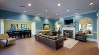 This single-floor space offers a thoughtfully designed interior that balances comfort and style. The main living area is anchored by a classic white fireplace, above which a decorative horse figurine adds a charming focal point. A wall-mounted flat-screen TV is positioned nearby for convenient viewing. The room features rich hardwood flooring throughout, paired with teal-painted walls and crisp white crown molding that create a vibrant yet polished atmosphere. Recessed lighting is evenly distributed across the ceiling, providing bright, even illumination throughout the space. A large, dark leather sectional sofa sits atop a neutral area rug, offering ample seating. Decorative elements include framed artwork, potted plants, and a round mirror, contributing to the room's well-curated aesthetic. An open doorway connects the living area to an adjacent room finished in soft green tones, which appears to function as a workspace or multipurpose area, complete with dark furniture and computer equipment. The seamless flow between rooms and the cohesive design choices make this a functional and welcoming space.
