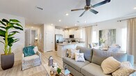 This two-floor home embraces a relaxed coastal aesthetic, with light wood-style flooring, crisp white walls, and beach-inspired décor woven throughout. A welcoming entryway hallway sets the tone, adorned with ocean-themed artwork and a whitewashed console table, leading into the main living areas. The open-concept living room and kitchen form the heart of the home, where a ceiling fan overhead and recessed lighting create a bright, airy atmosphere. The kitchen is well-appointed with white shaker-style cabinetry, granite countertops, a peninsula with seating, stainless steel appliances including a French door refrigerator, range, microwave, and dishwasher — all complemented by a deep undermount sink. A dedicated dining area sits adjacent, completing the open layout. The bedrooms carry the coastal theme forward; one features a bunk bed setup ideal for multiple guests, while another offers a queen bed with a teal-framed headboard and a double closet. Bathrooms include white vanities with granite countertops and walk-in shower enclosures. A secondary living or flex space on the second floor provides additional room for lounging or entertaining, accented by tropical greenery and natural textures throughout.