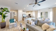 This two-floor home embraces a relaxed coastal aesthetic, with light wood-style flooring, crisp white walls, and beach-inspired décor woven throughout. A welcoming entryway hallway sets the tone, adorned with ocean-themed artwork and a whitewashed console table, leading into the main living areas. The open-concept living room and kitchen form the heart of the home, where a ceiling fan overhead and recessed lighting create a bright, airy atmosphere. The kitchen is well-appointed with white shaker-style cabinetry, granite countertops, a peninsula with seating, stainless steel appliances including a French door refrigerator, range, microwave, and dishwasher — all complemented by a deep undermount sink. A dedicated dining area sits adjacent, completing the open layout. The bedrooms carry the coastal theme forward; one features a bunk bed setup ideal for multiple guests, while another offers a queen bed with a teal-framed headboard and a double closet. Bathrooms include white vanities with granite countertops and walk-in shower enclosures. A secondary living or flex space on the second floor provides additional room for lounging or entertaining, accented by tropical greenery and natural textures throughout.